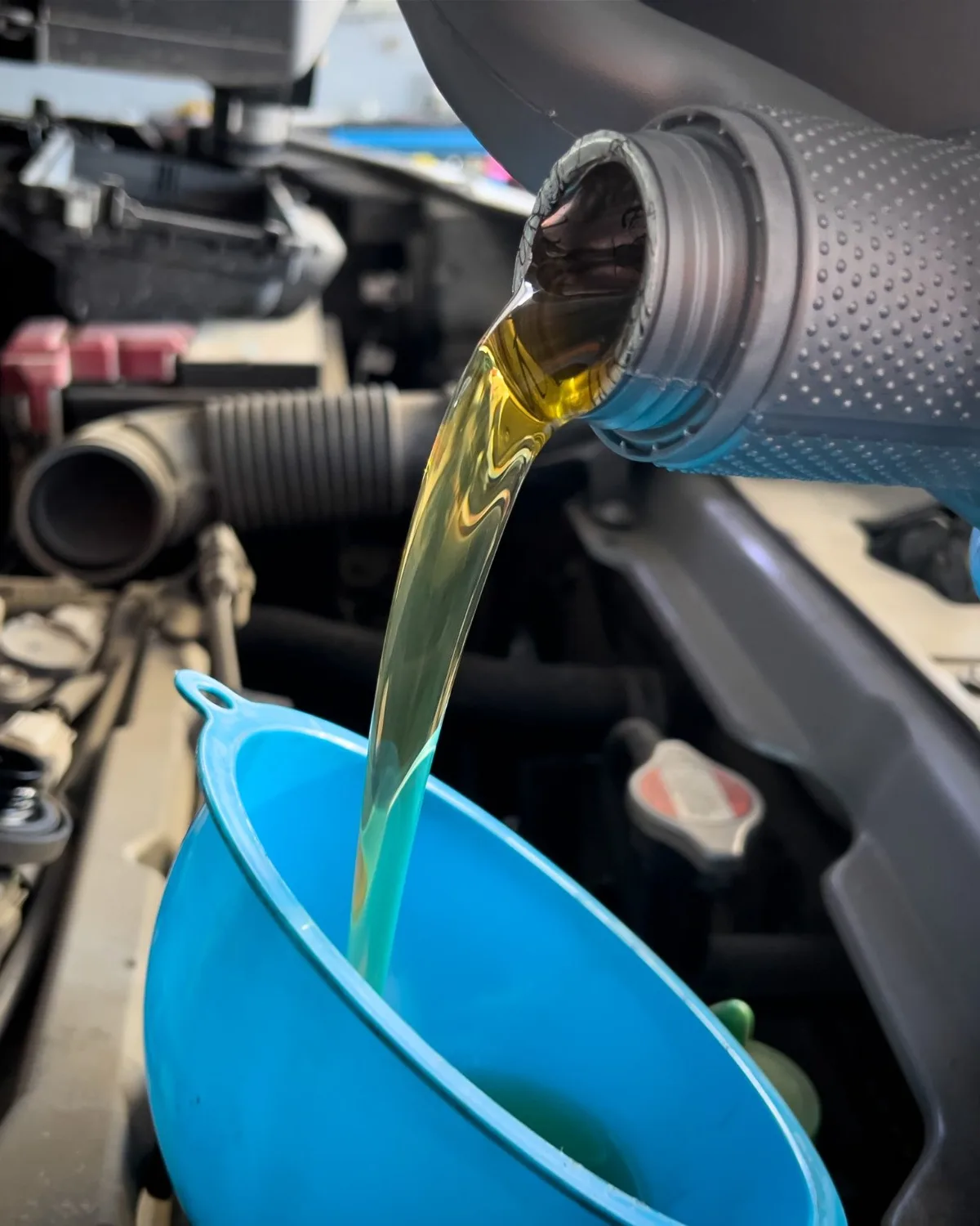 Fresh motor oil pouring from a bottle into a funnel over an open engine