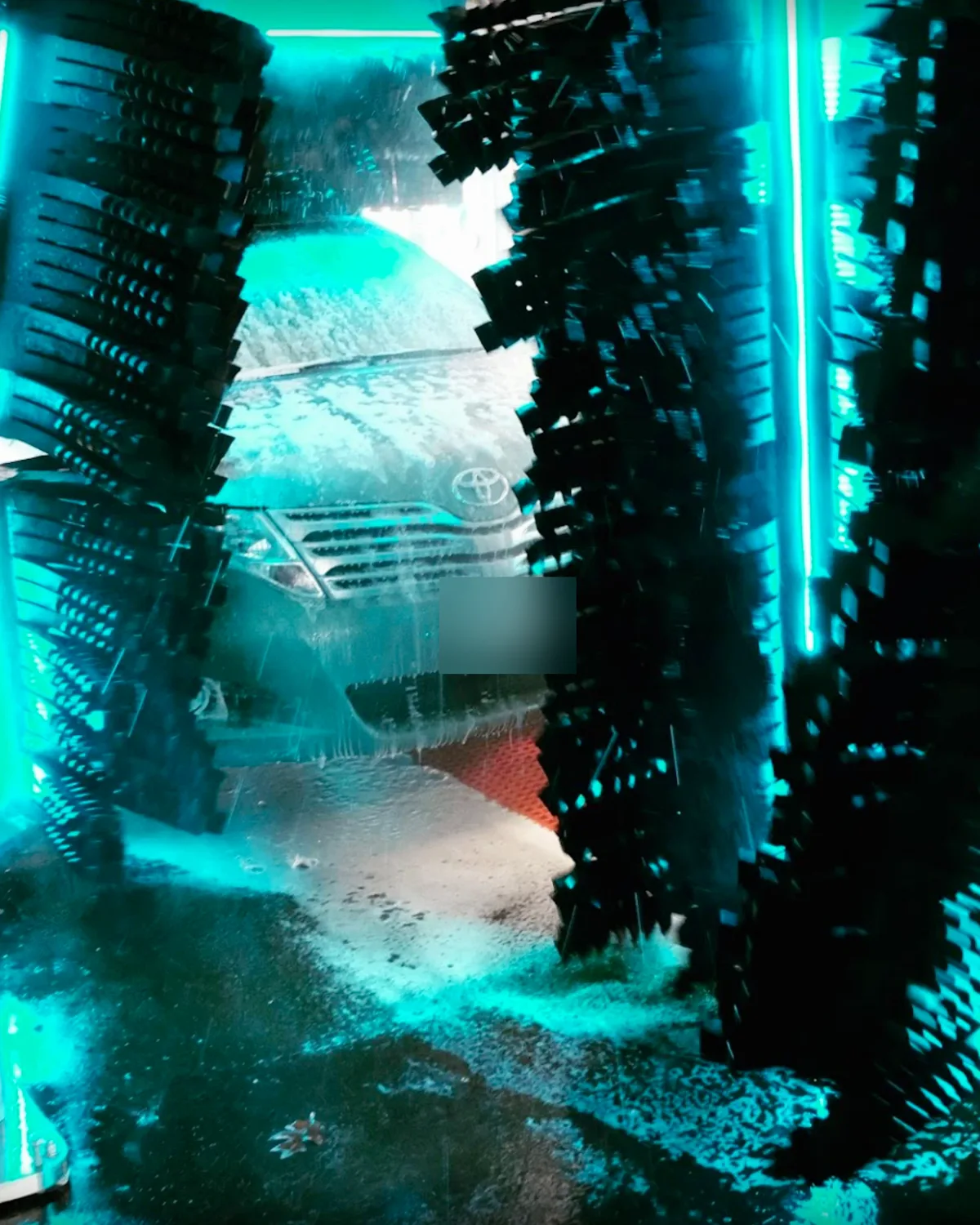 A car in the foam between the spinning brushes of a Platinum wash tunnel, lit in teal